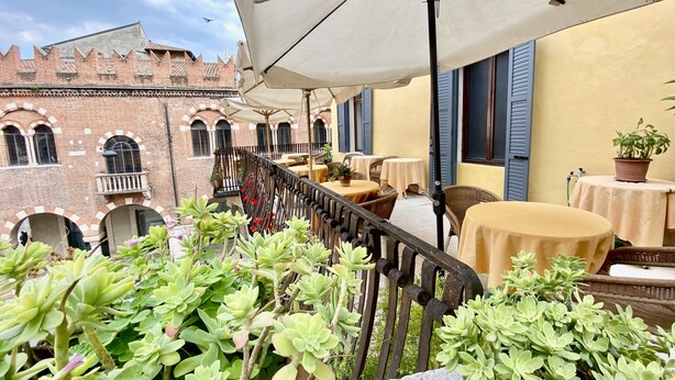 A terrace with outdoor seating, a wrought iron railing, and potted plants. - Hotel Aurora (Verona)