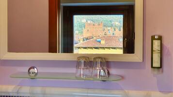 Une salle de bain avec une fenêtre donnant sur un château, un distributeur de savon et un porte-savon en verre.