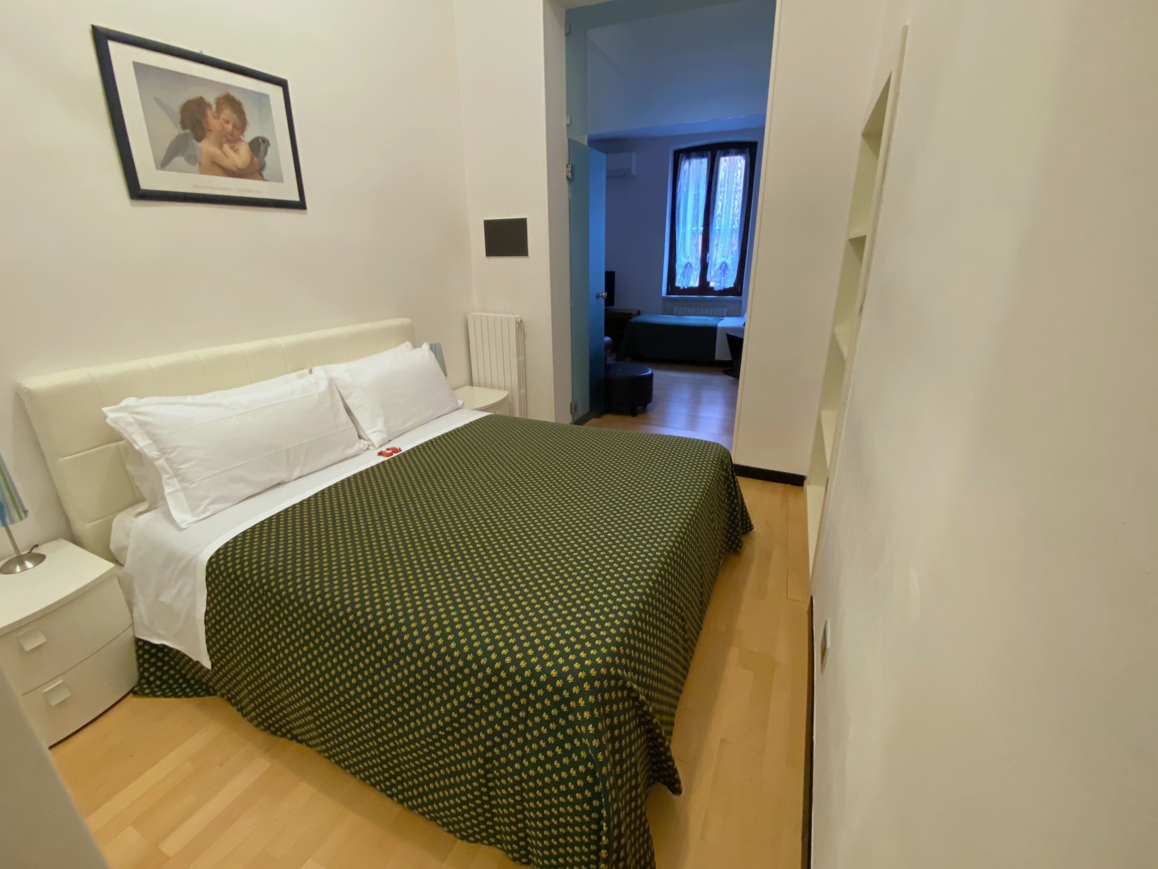 Un dormitorio con una cama, una mesita de noche blanca y un cuadro en la pared.