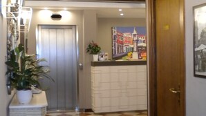 A hallway with a checkered floor, a wooden ceiling, a reception desk, and a door. - Hotel Aurora (Verona)