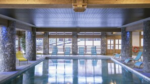 An indoor swimming pool with stone pillars, blue chairs, and large windows. - CGH  La Grange aux Fées (Les Avanchers-Valmorel)