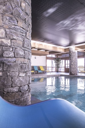 Un espace piscine agrémenté de piliers en pierre, d’un toboggan bleu et de chaises longues jaunes et bleues.
