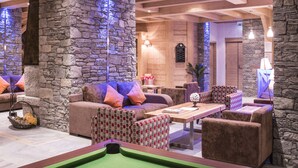 A pool table with balls and cues, surrounded by sofas and chairs in a room with stone walls and wooden beams. - CGH  La Grange aux Fées (Les Avanchers-Valmorel)