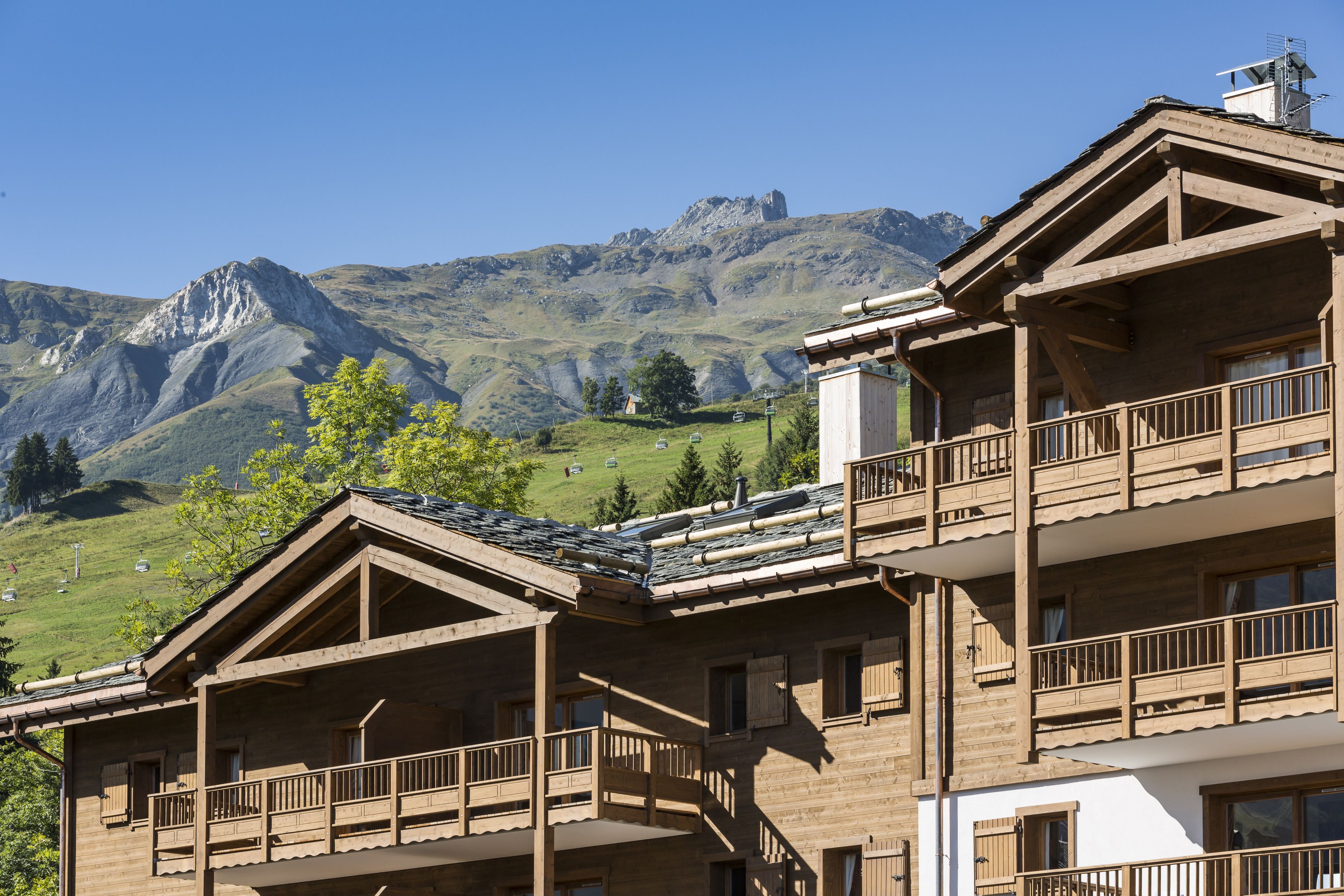 A wooden chalet with balconies, set against a mountainous backdrop.