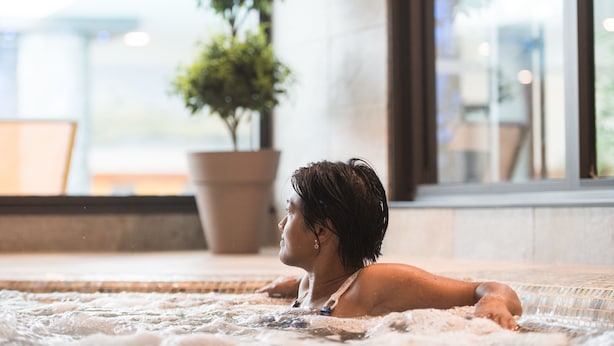 A person relaxing in a hot tub with a view of a potted plant and a modern interior. - CGH Résidences Boutique Le Napoléon (Montgenevre)