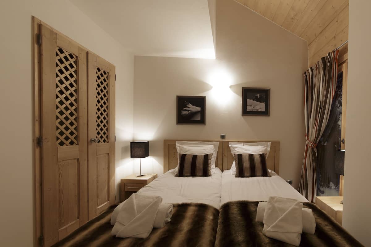 A double bed with white linens, a wooden headboard, and a fur throw. There are two bedside tables with lamps.