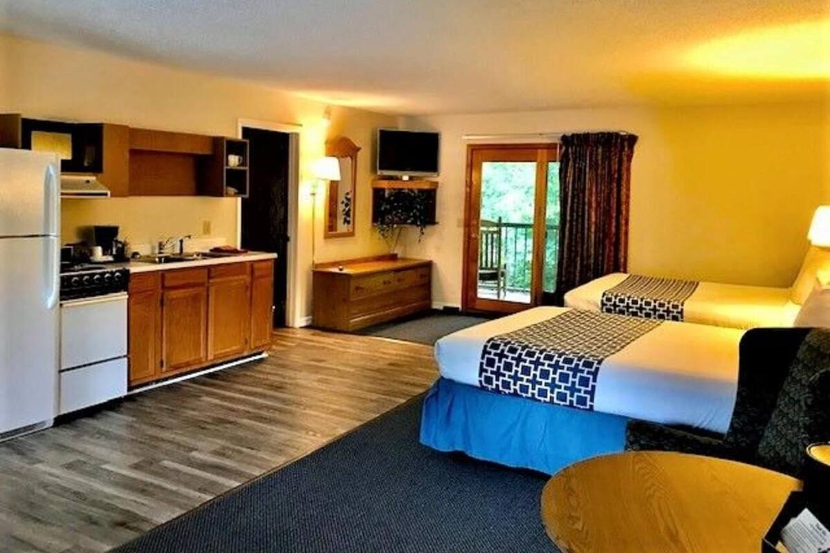 A hotel room with a kitchenette, two beds, a TV, and a balcony with curtains.