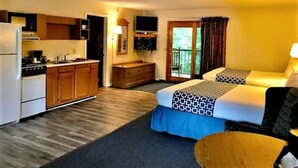 Une chambre d’hôtel avec une kitchenette, deux lits, une télévision et un balcon avec des rideaux.