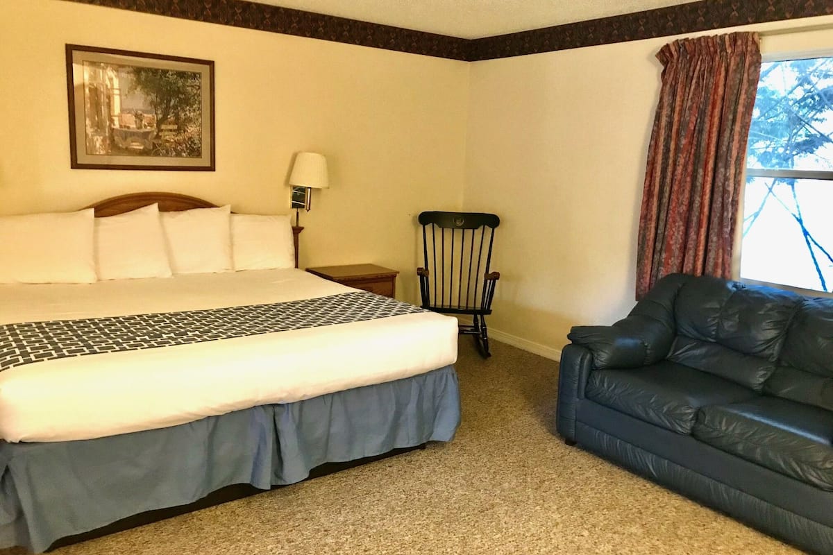 A hotel room with a large bed, a chair, a couch, and a window with curtains.