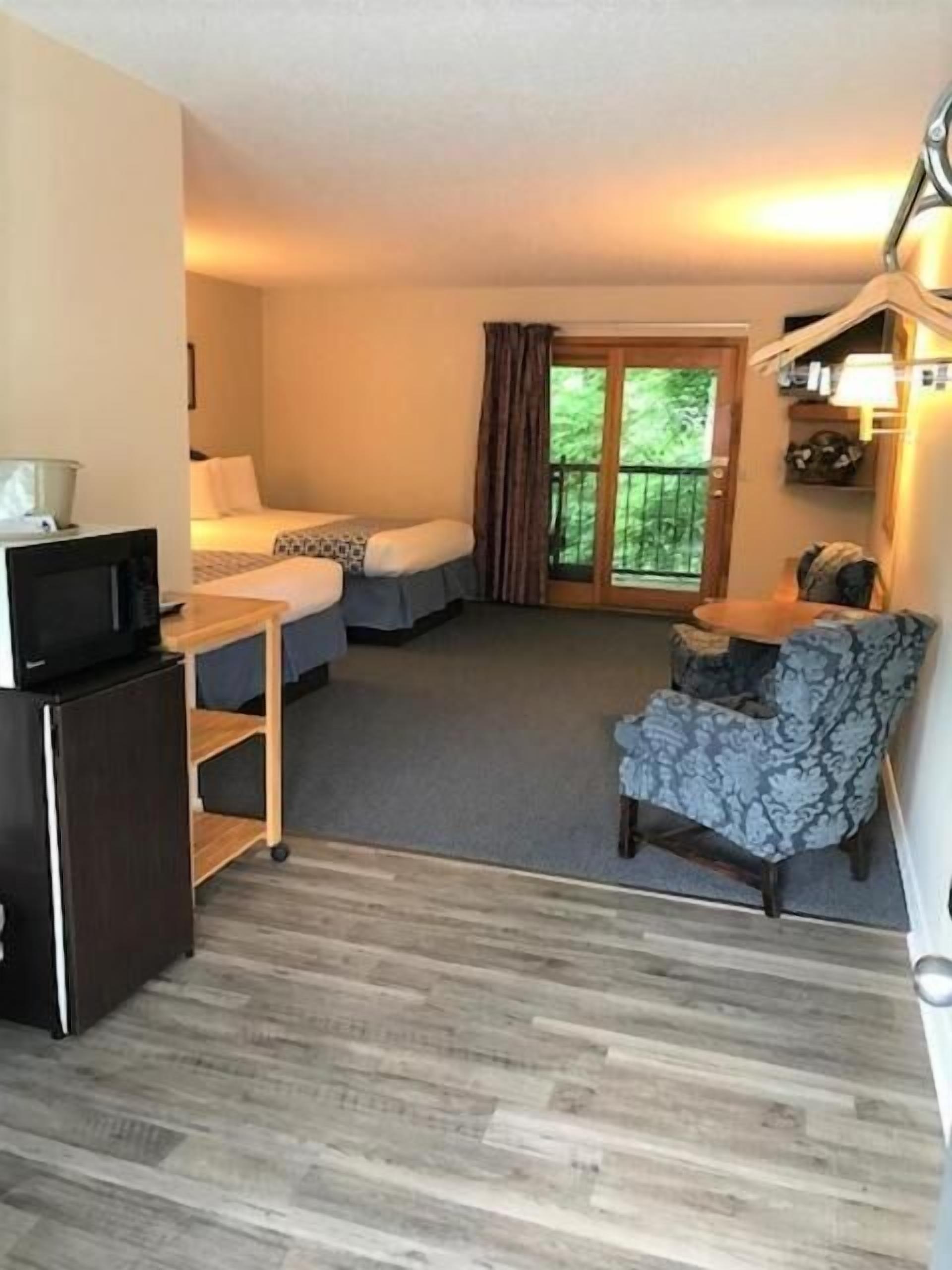 A hotel room with a bed, a desk, a chair, a small refrigerator, and a sliding glass door to the outside.