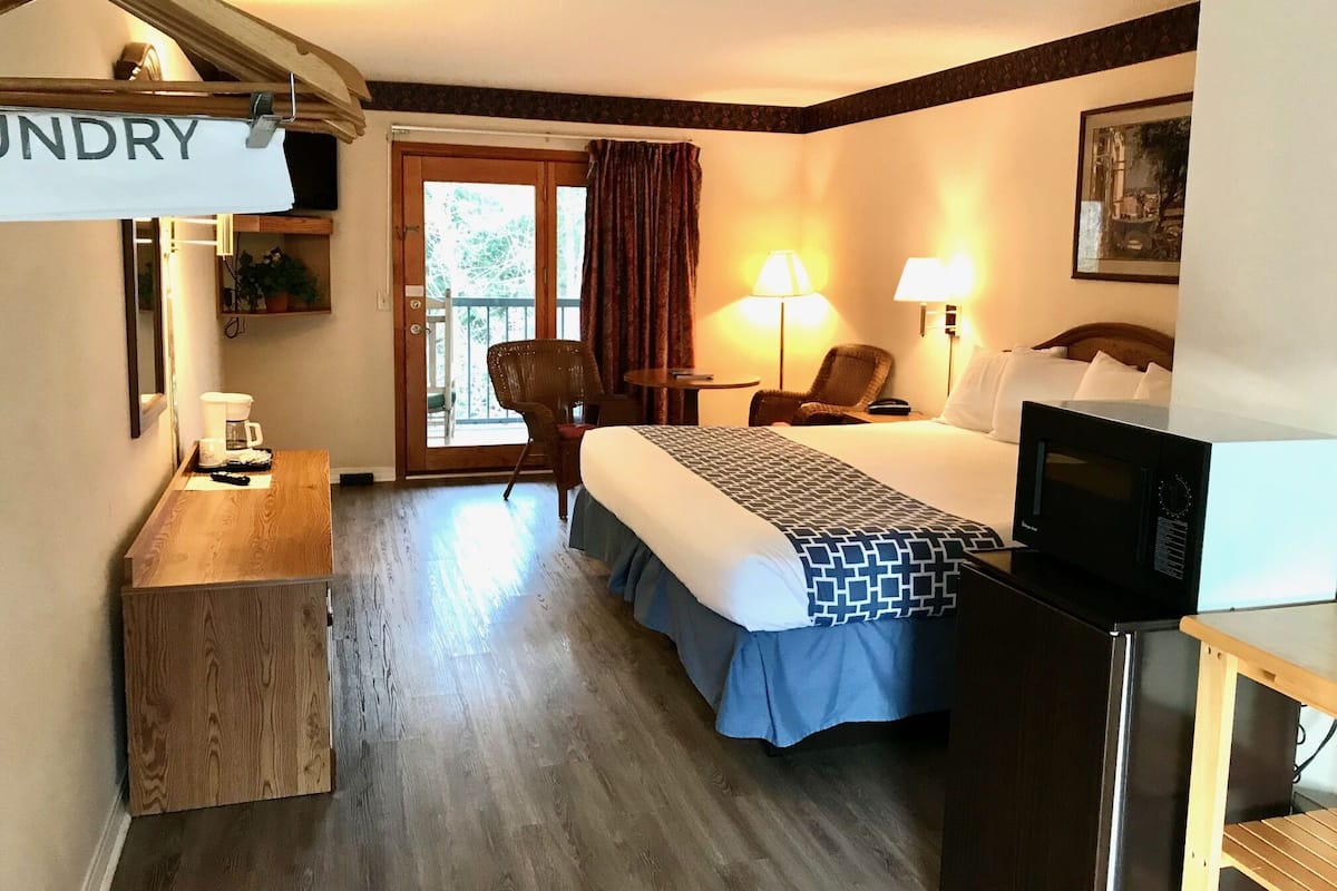A hotel room with a bed, a desk with a coffee maker, a chair, a TV, and a sign that reads "LINDRY".