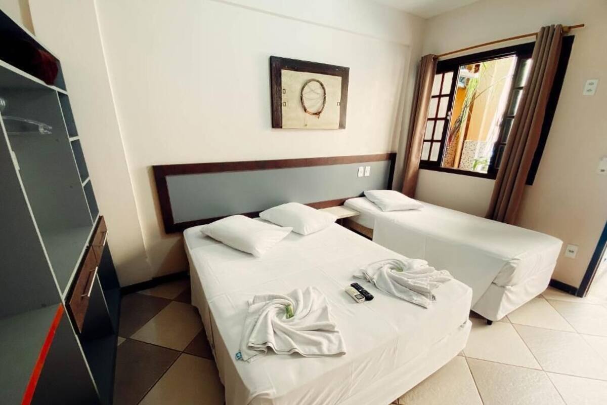 A hotel room with two beds, a wardrobe, a window with curtains, and a wall-mounted artwork.