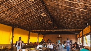 Uma área de refeições ao ar livre com móveis de vime e um telhado de palha.