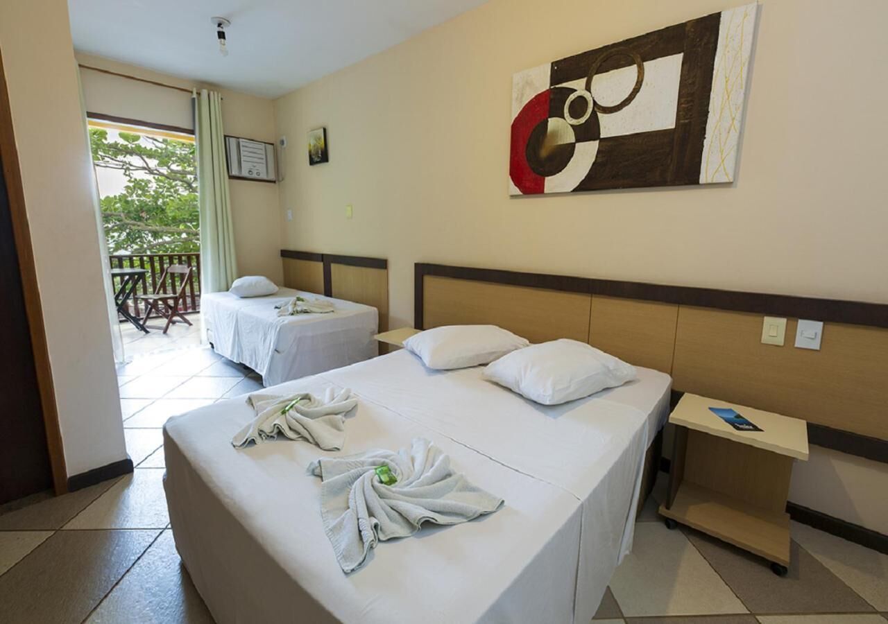Quarto de hotel com duas camas, uma mesinha e um quadro na parede.