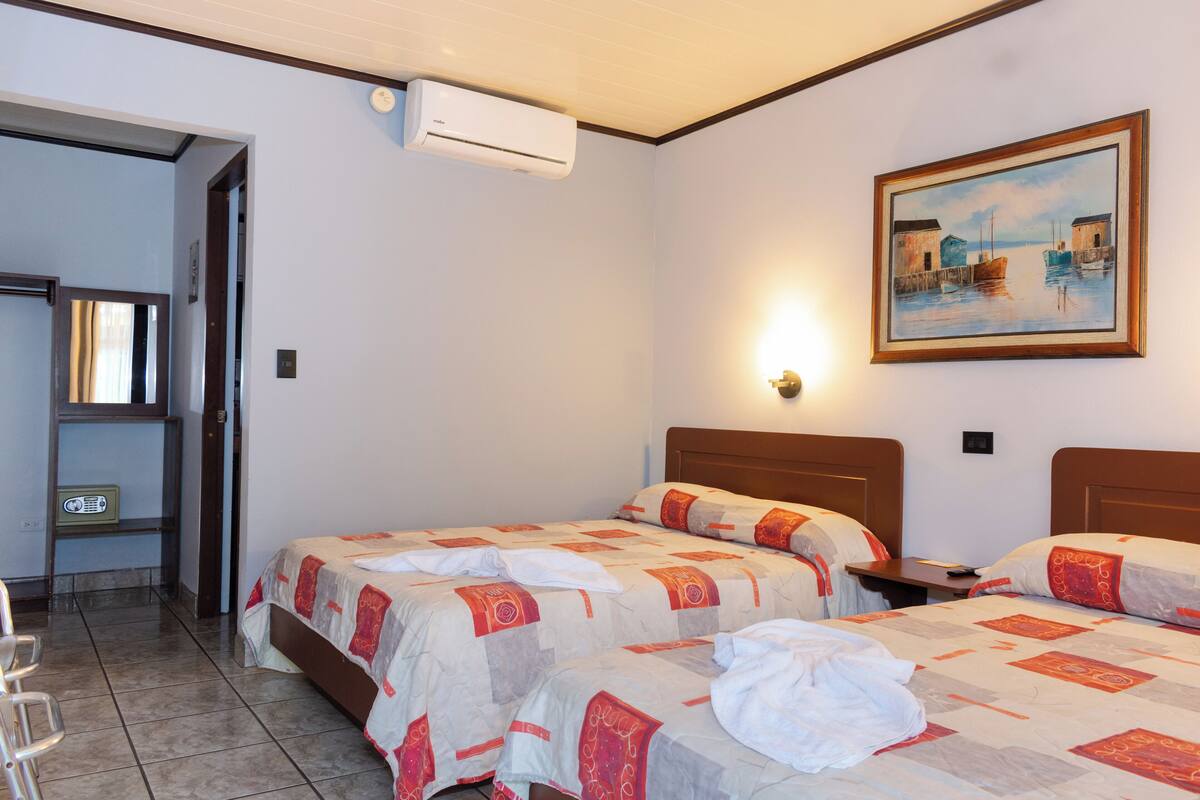 A hotel room with two beds, a painting on the wall, and an air conditioning unit.