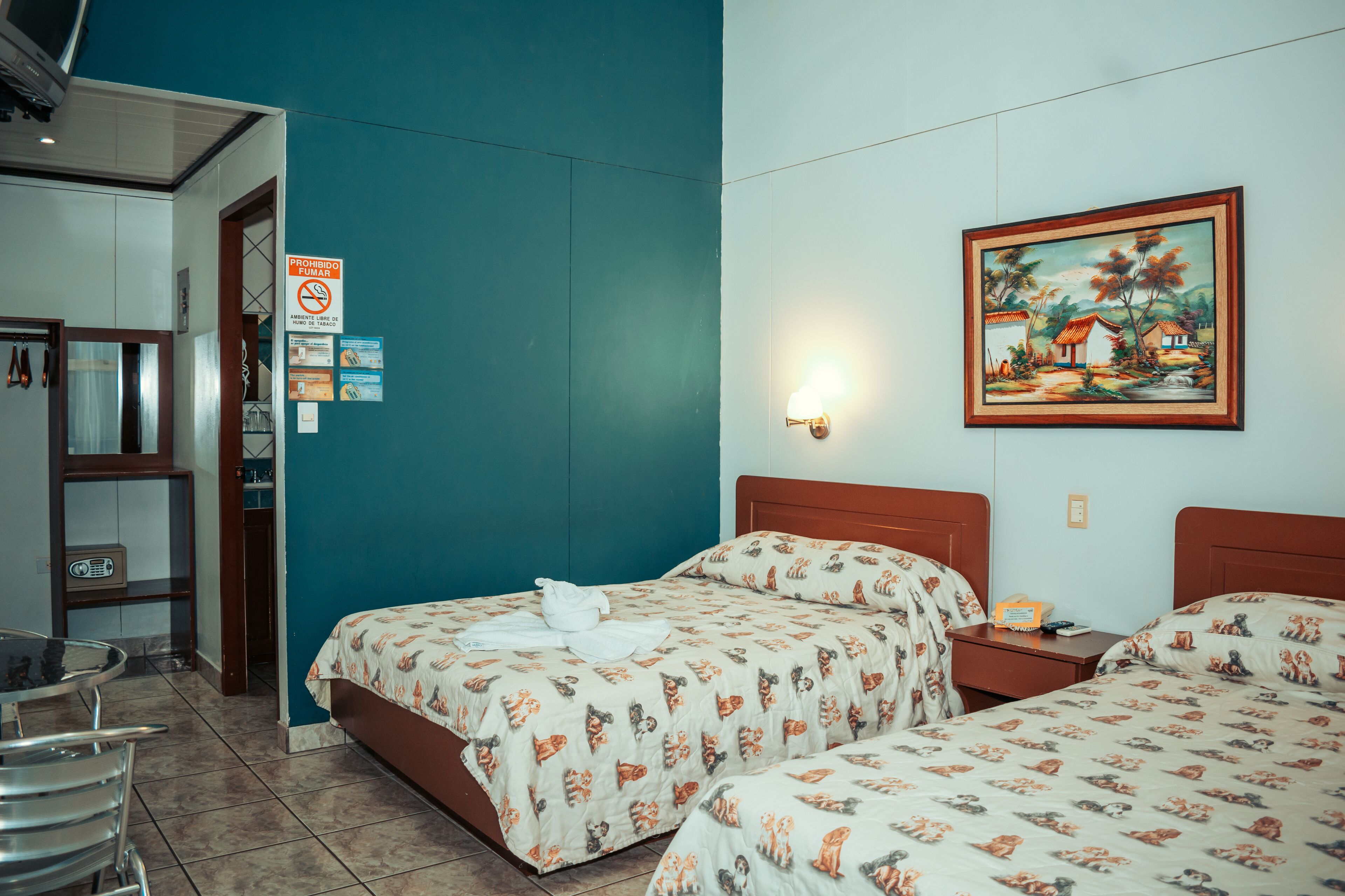 A hotel room with two beds, a painting on the wall, and a sign prohibiting smoking.