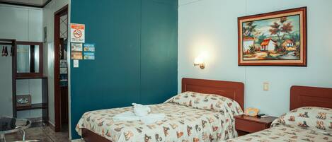 A hotel room with two beds, a painting on the wall, and a sign prohibiting smoking.