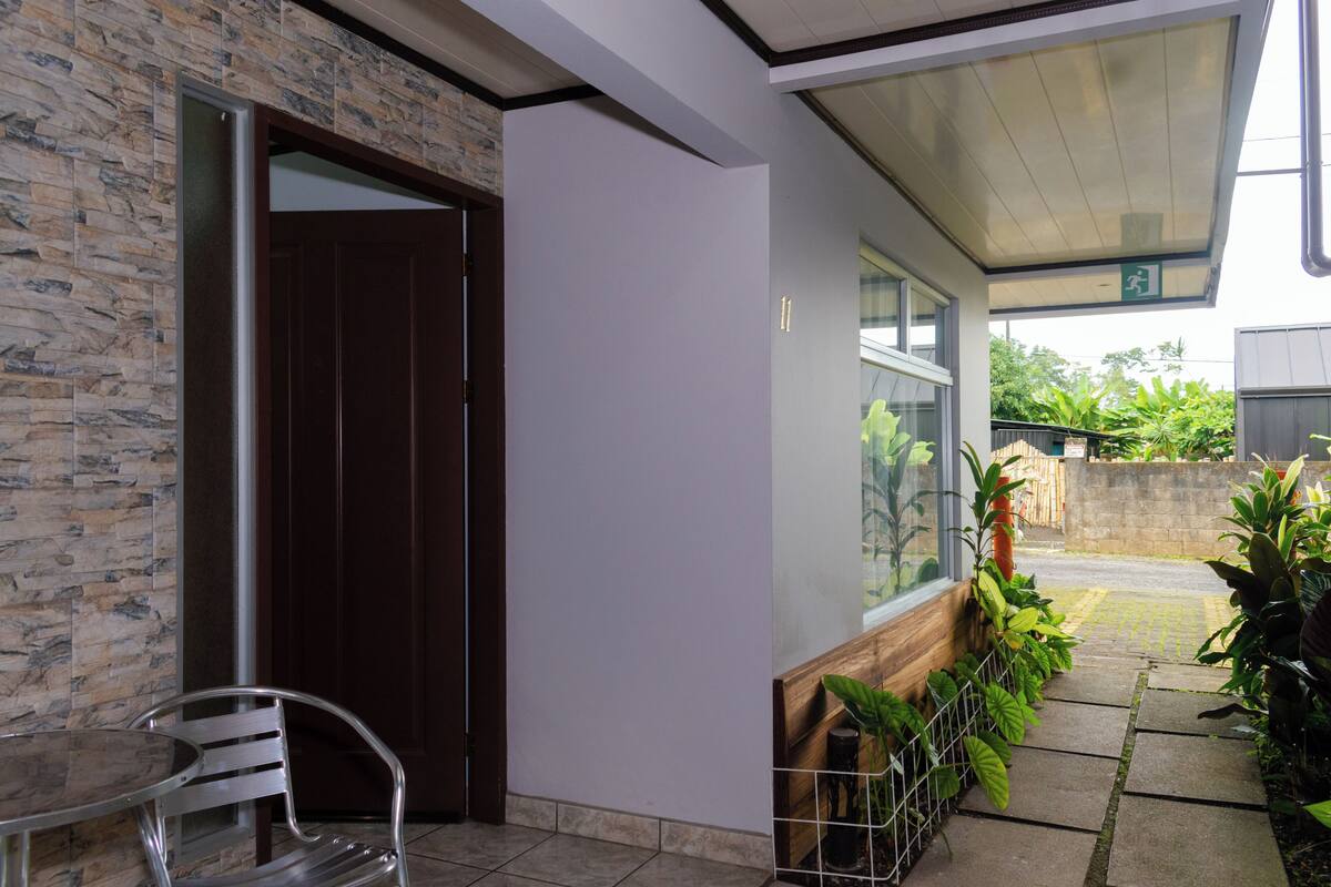 A building entrance with a stone wall, a wooden door, and a covered patio area with potted plants.