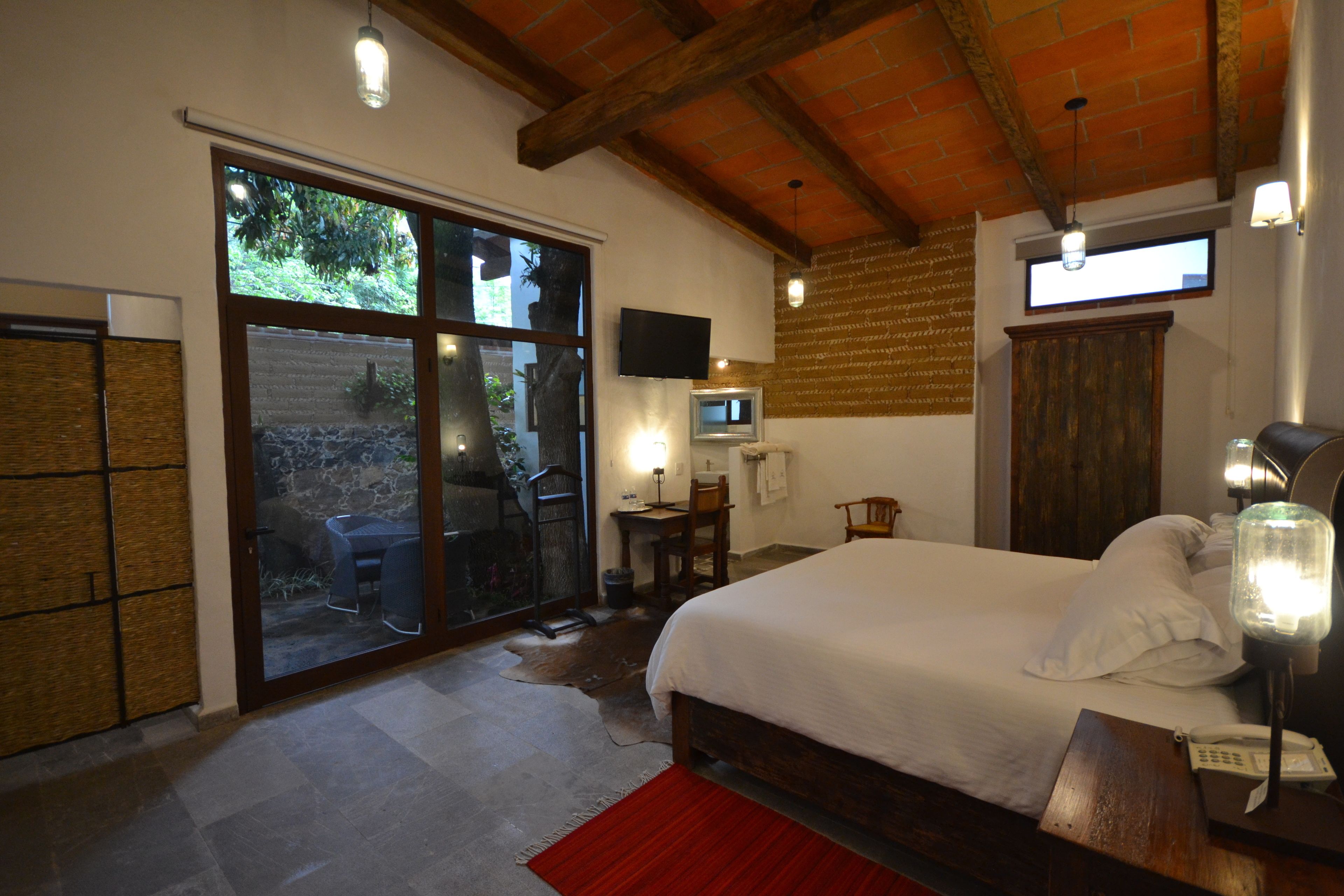 A bedroom with a large bed, a TV mounted on the wall, and a sliding glass door leading to an outdoor area.