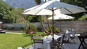 Un espace de restauration en plein air, avec des tables et des parasols, entouré d’une pelouse bien entretenue et d’un mur de pierres.