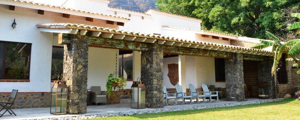 Une terrasse couverte avec des piliers en pierre, des sièges d’extérieur et une vue sur la végétation environnante.