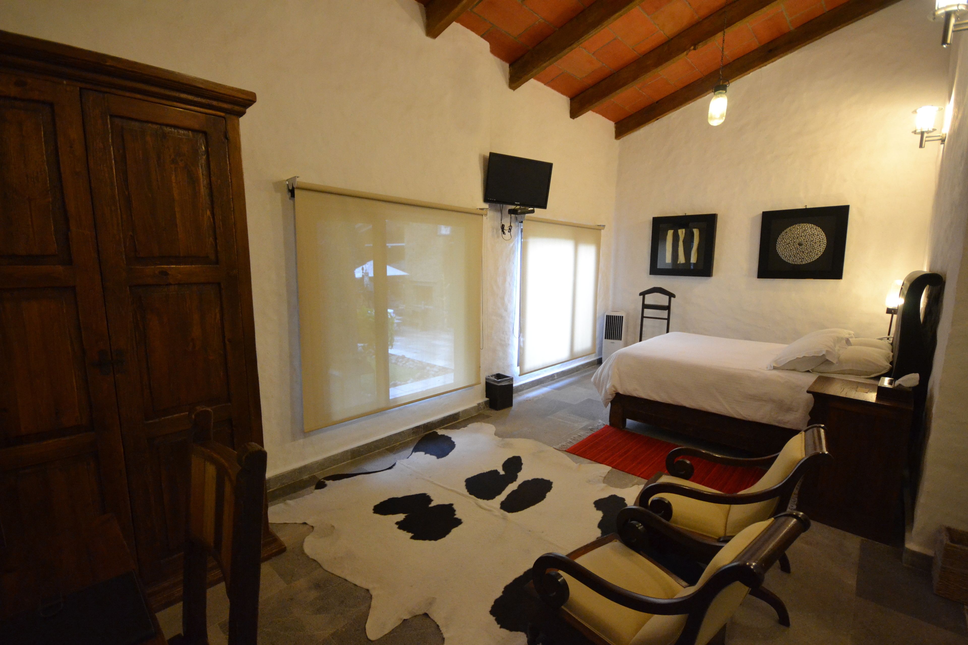 A bedroom with a bed, a wooden wardrobe, a television, and a window with blinds.