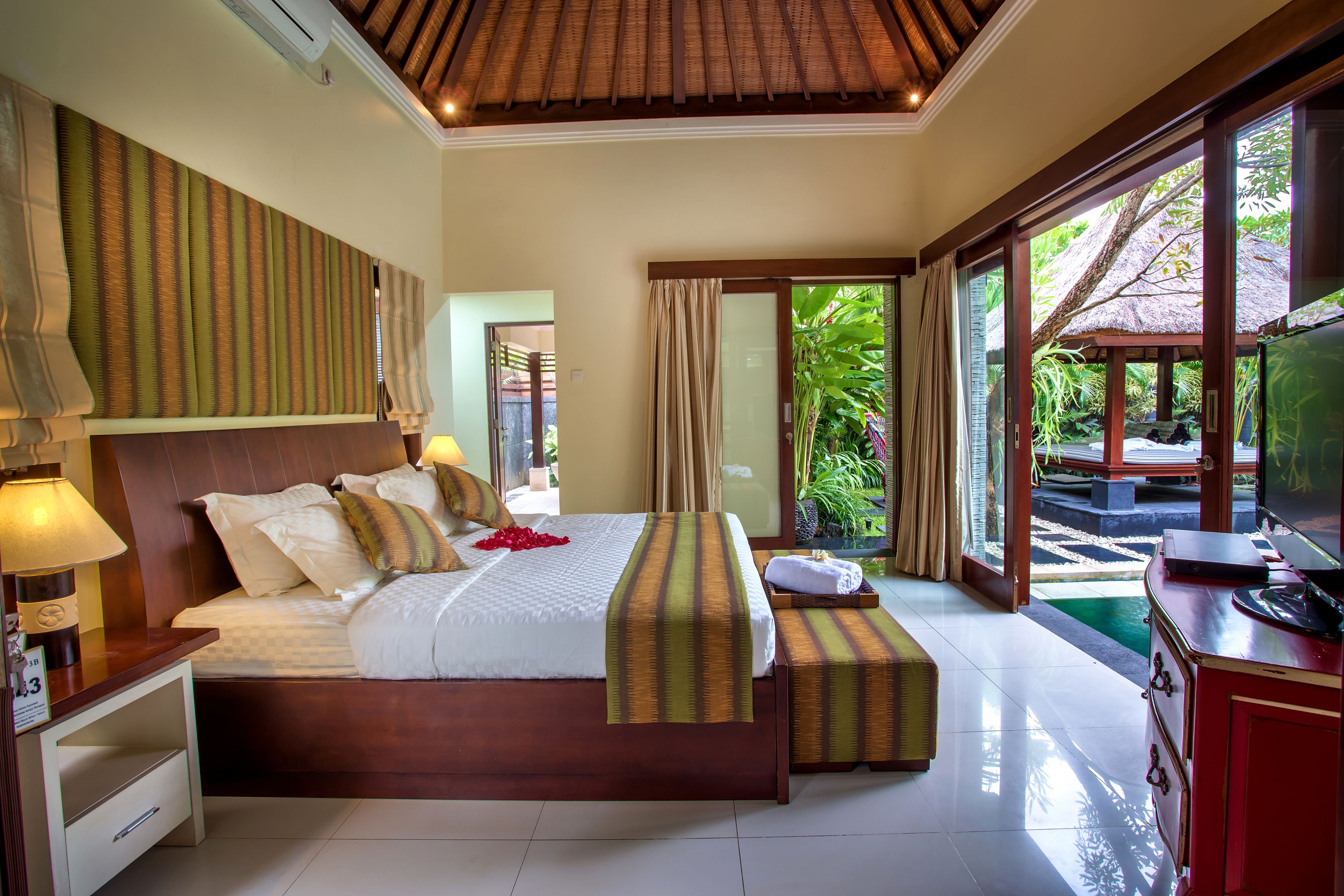 A well-appointed bedroom with a large bed, bedside tables, a TV, and a view of the garden.