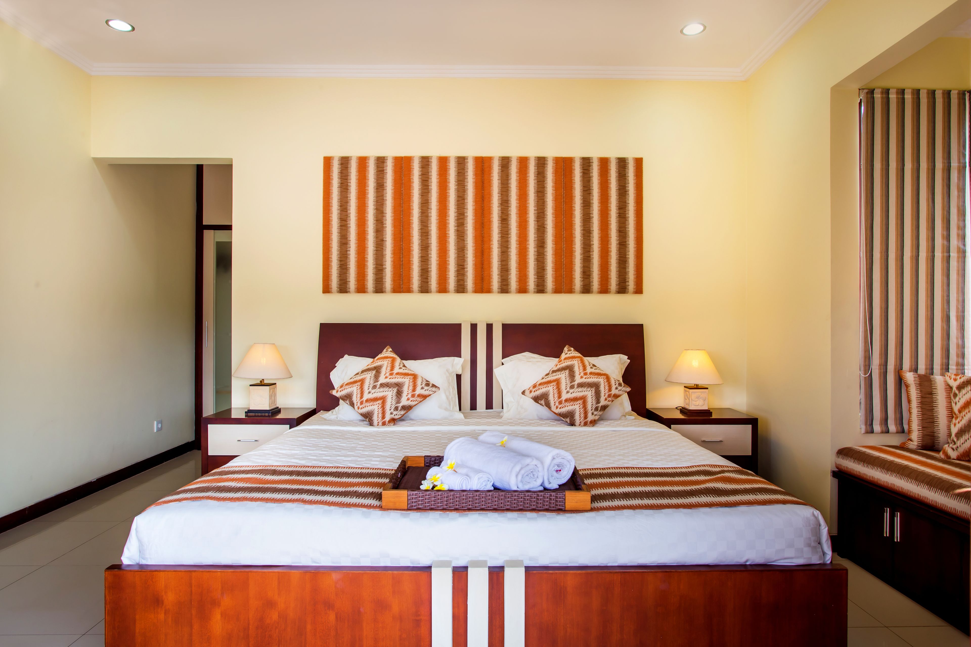 A hotel room with a large bed, two nightstands, a wall-mounted artwork, and a striped curtain.