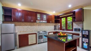 Une cuisine moderne avec des meubles en bois, un îlot central, des appareils électroménagers en acier inoxydable et une fenêtre donnant sur un paysage verdoyant.