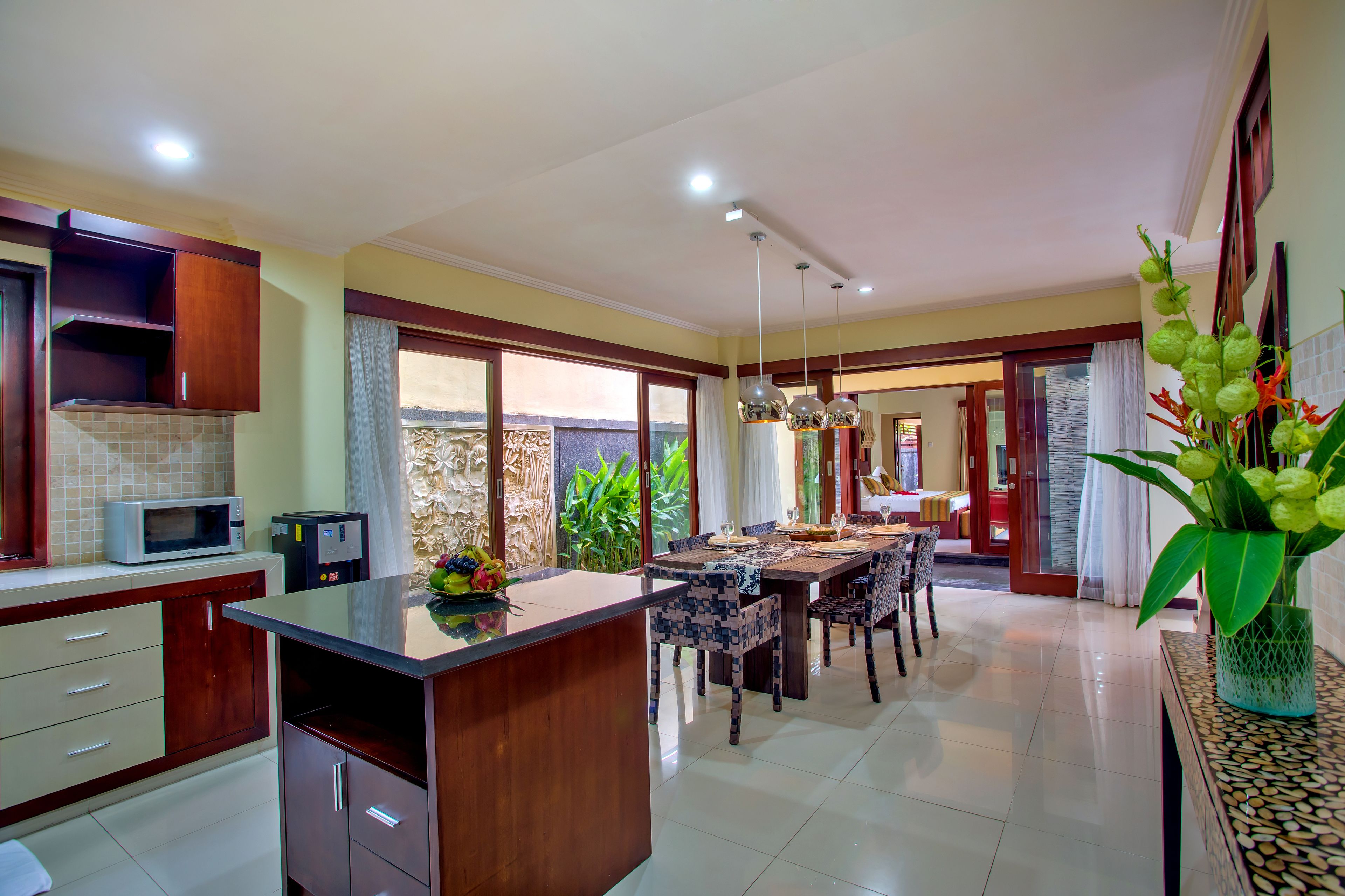 A modern kitchen with a central island, dining area with chairs, and a view of the outside.