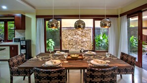 Un coin repas avec une table en bois dressée pour quatre personnes, entourée de chaises à motifs, avec un mur décoratif et des plantes en arrière-plan.