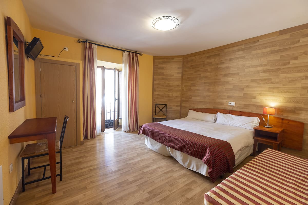 Une chambre d’hôtel avec un plancher en bois, un lit recouvert d’une courtepointe rouge et blanche, un bureau avec une chaise, une table de chevet avec une lampe et une tête de lit en bois.