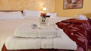 Een net opgemaakt bed met witte lakens, een fles Orquidea douchegel en een gevouwen witte handdoek op het bed.