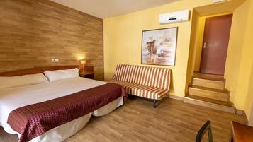 Habitación de hotel con una cama grande, una silla a rayas, un cuadro en la pared y una escalera que conduce a un piso superior.