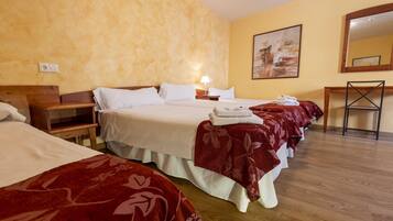 A hotel room with three beds, each with a red floral bedspread, a wooden nightstand, a bedside table, and a wall-mounted painting.