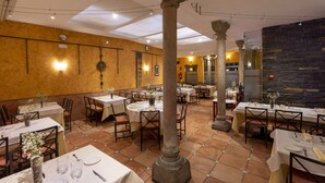 Een restaurant met meerdere tafels, stenen zuilen en een betegelde vloer.