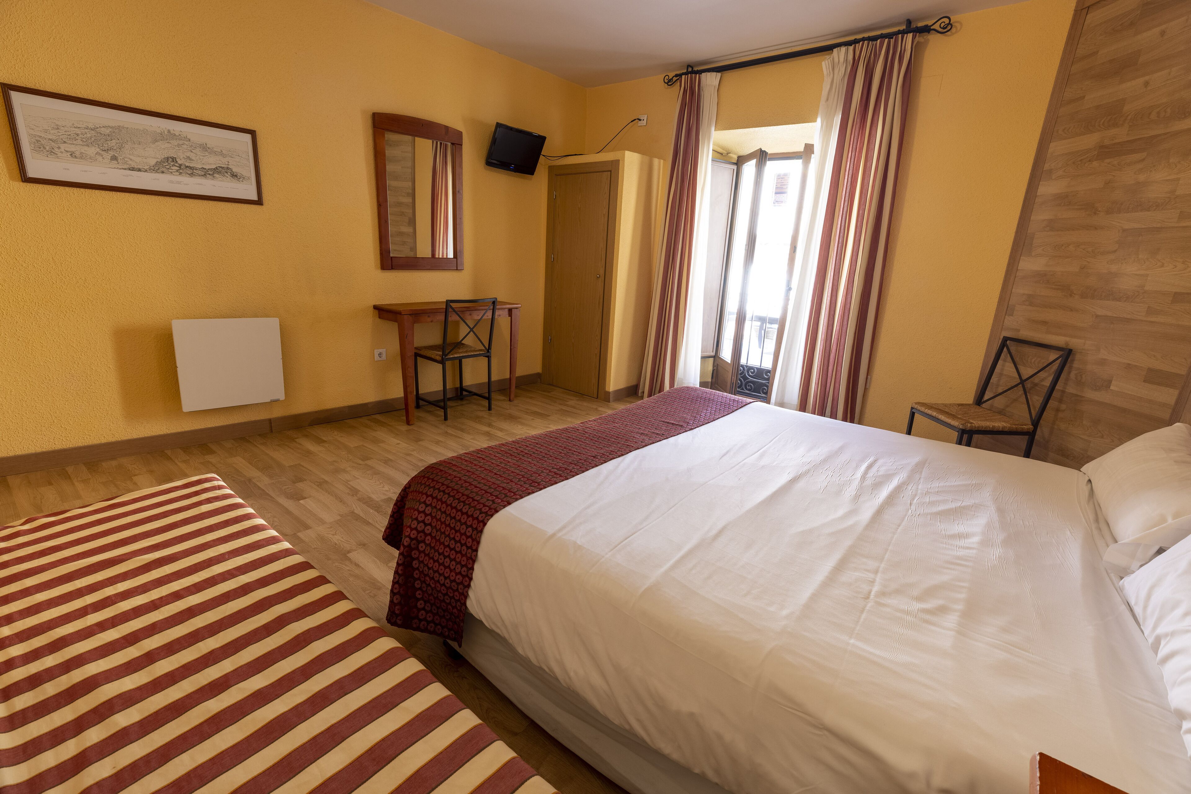 Habitación de hotel con una cama grande, un escritorio, una silla, un televisor y una ventana con cortinas.