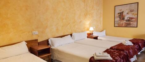 A hotel room with four beds, a wooden headboard, a nightstand with a lamp, and a painting on the wall.