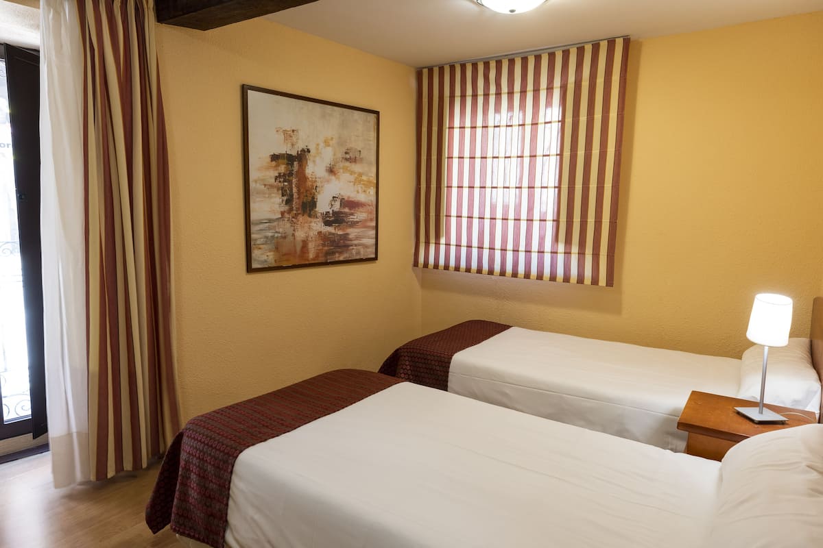 Une chambre d’hôtel avec deux lits, un tableau au mur, une fenêtre avec des rideaux à rayures et une lampe de chevet.