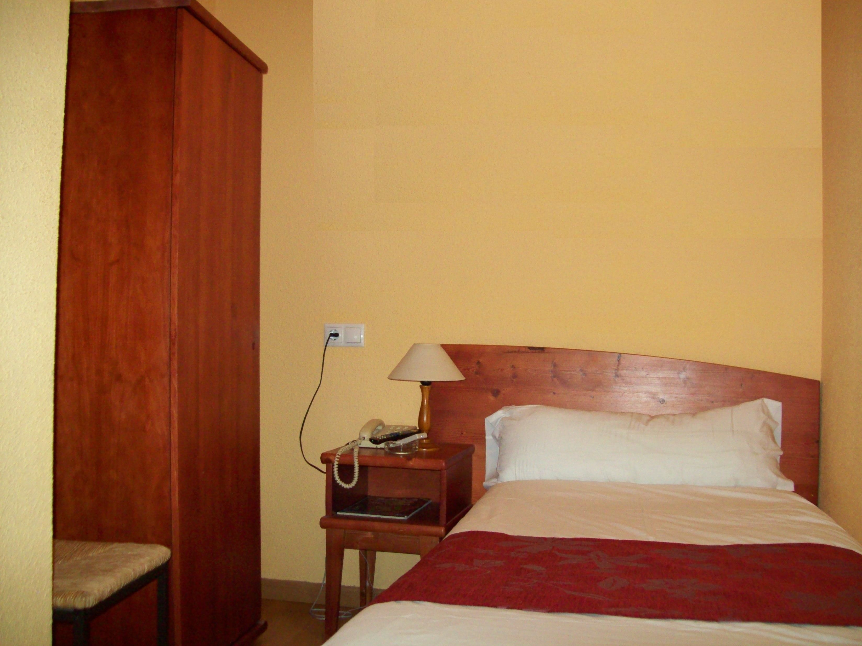 Een hotelkamer met een houten hoofdeinde, een nachtkastje met een lamp, een telefoon en een rode plaid over het bed.