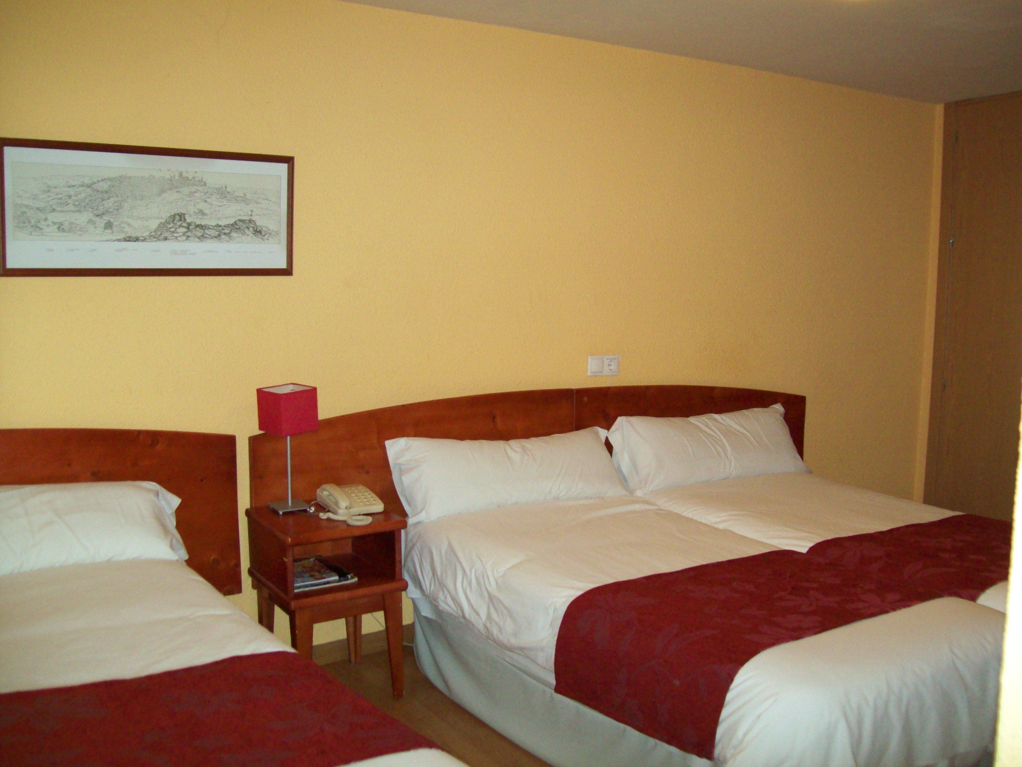 Habitación de hotel con dos camas, una mesita de noche con teléfono, lámpara y un cuadro en la pared.