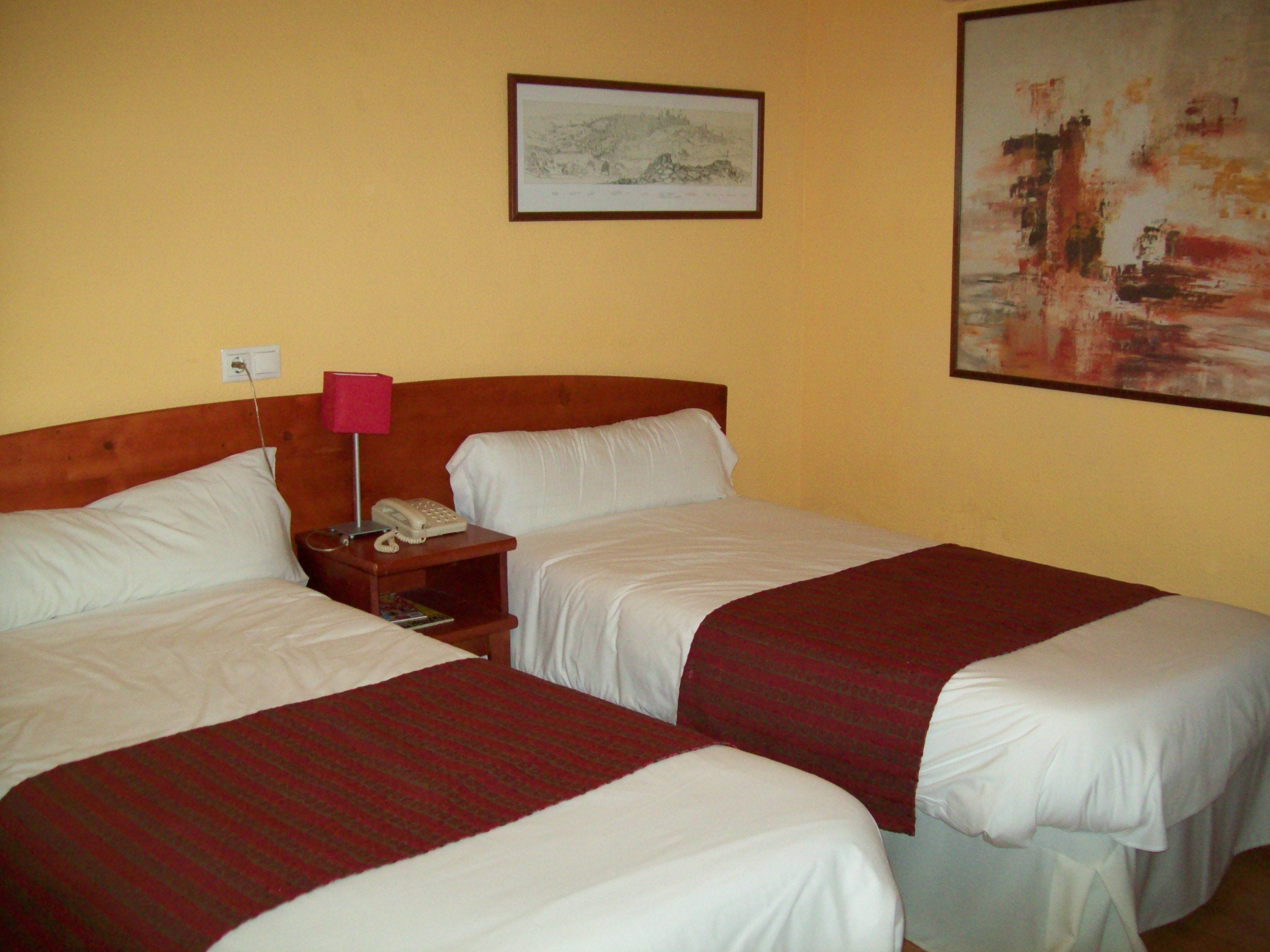 Una habitación de hotel con dos camas, una mesita de noche con teléfono y un cuadro en la pared.