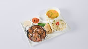 Una bandeja con diversos platos, incluyendo un bol de curry, arroz, un bol de sopa y un pequeño recipiente de chutney.