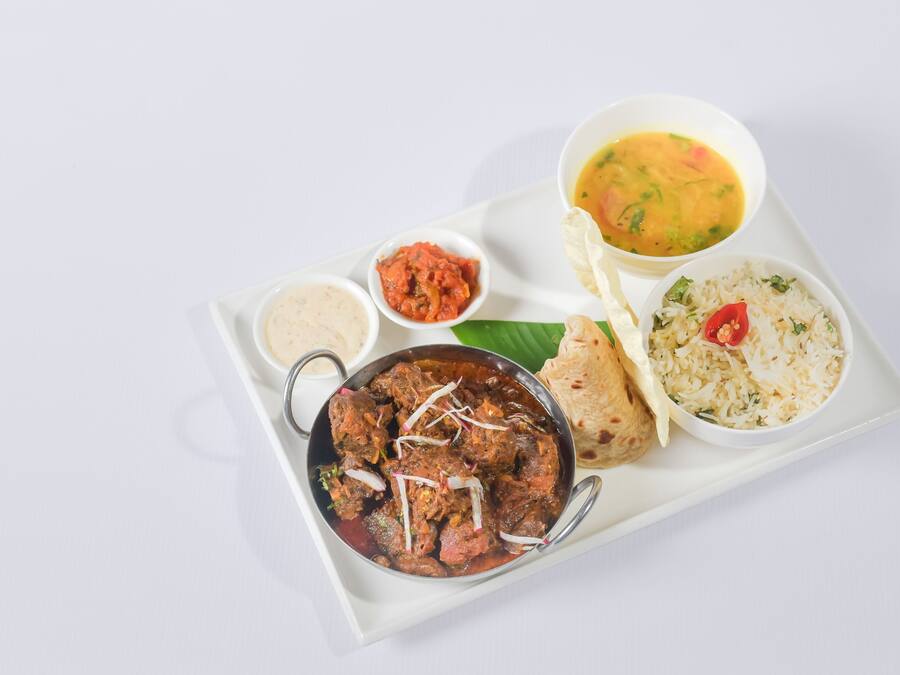 Una bandeja con diversos platos, incluyendo un bol de curry, arroz, un bol de sopa y un pequeño recipiente de chutney.