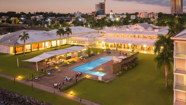 Een hotel met een zwembad, terras en uitzicht op de skyline in de schemering.
