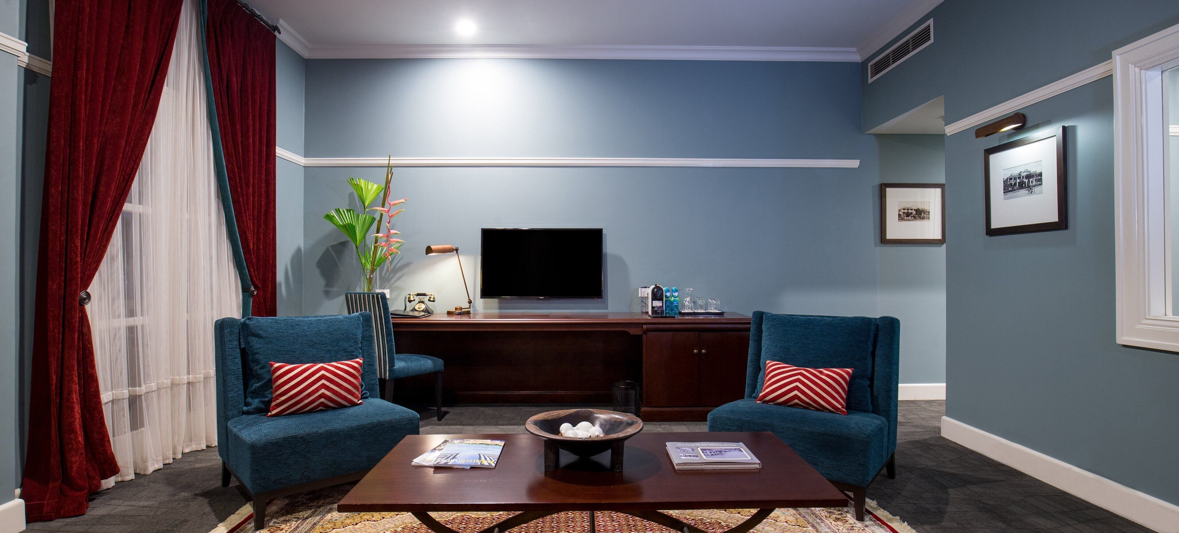 Un salón con dos sillones azules, una mesa de centro, un televisor y cuadros en la pared.