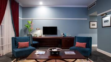 A living room with two blue armchairs, a coffee table, a TV, and framed pictures on the wall.