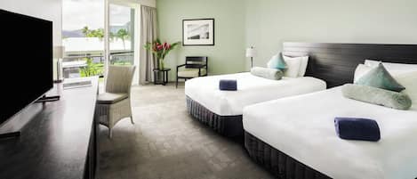 Een hotelkamer met twee bedden, een televisie, een stoel, een klein tafeltje en een raam met uitzicht op palmbomen.