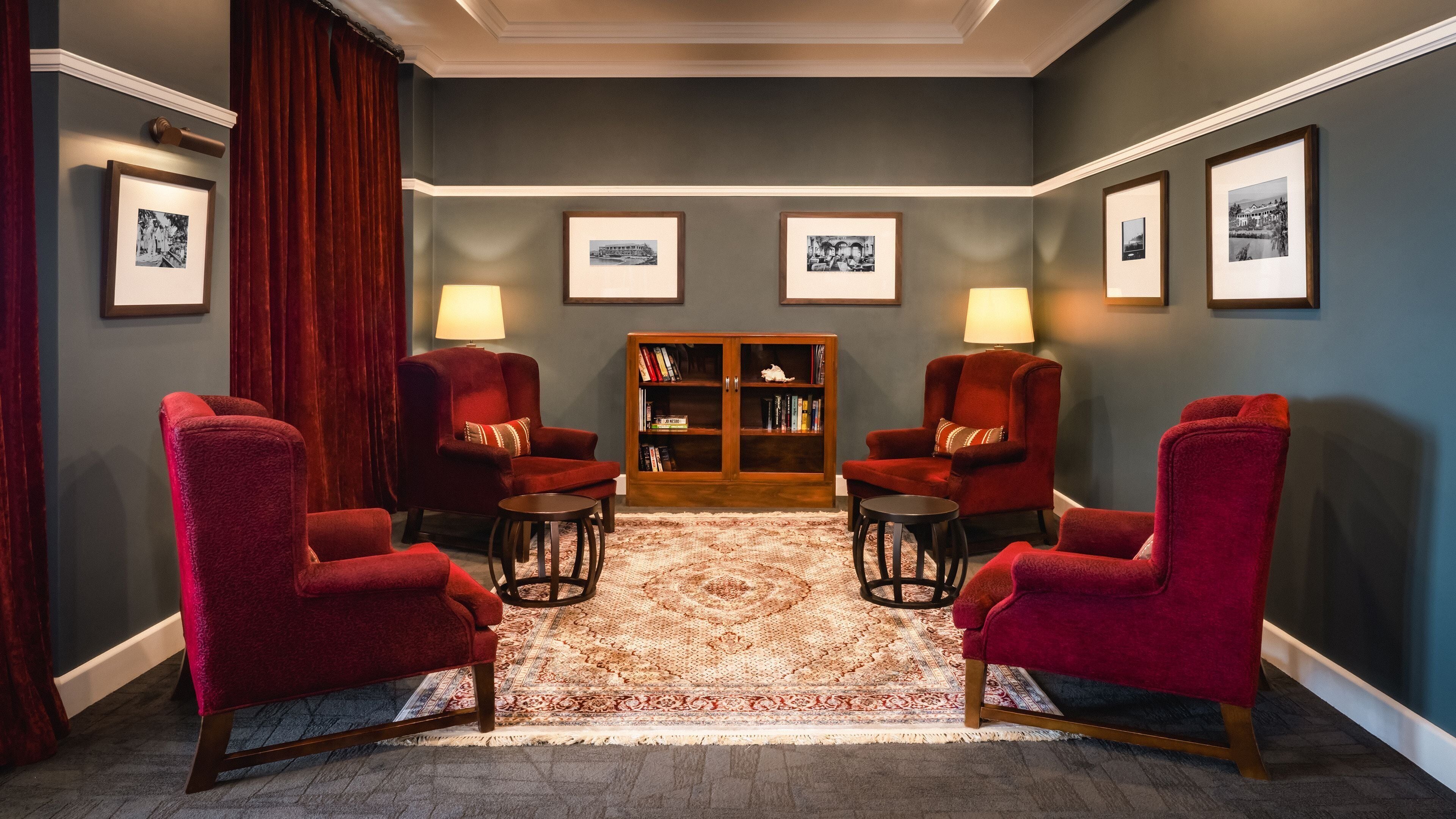 A room with four red armchairs, a wooden bookcase, and a patterned rug.