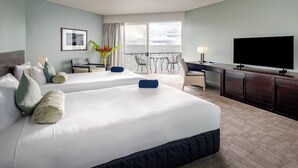 A hotel room with two beds, a desk, a TV, and a balcony with a view of the sea. - Grand Pacific Hotel Fiji (Suva)